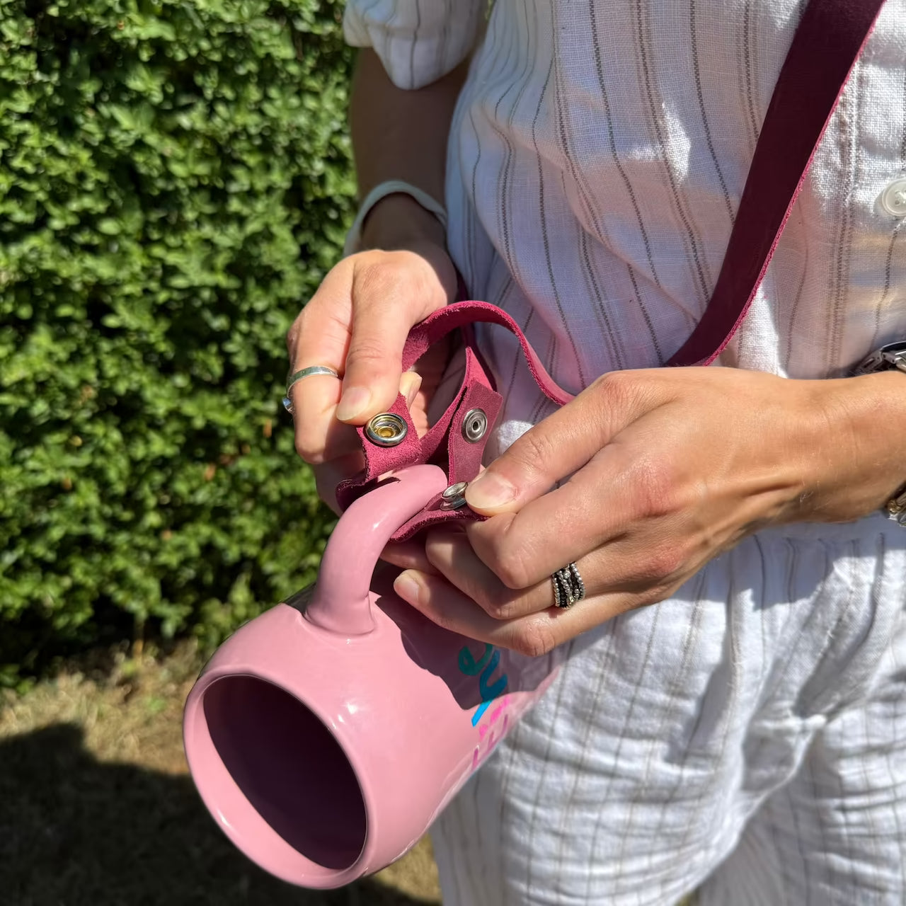 Model zeigt Druckknopfverschluss des magenta Lederbandes am rosa Krug