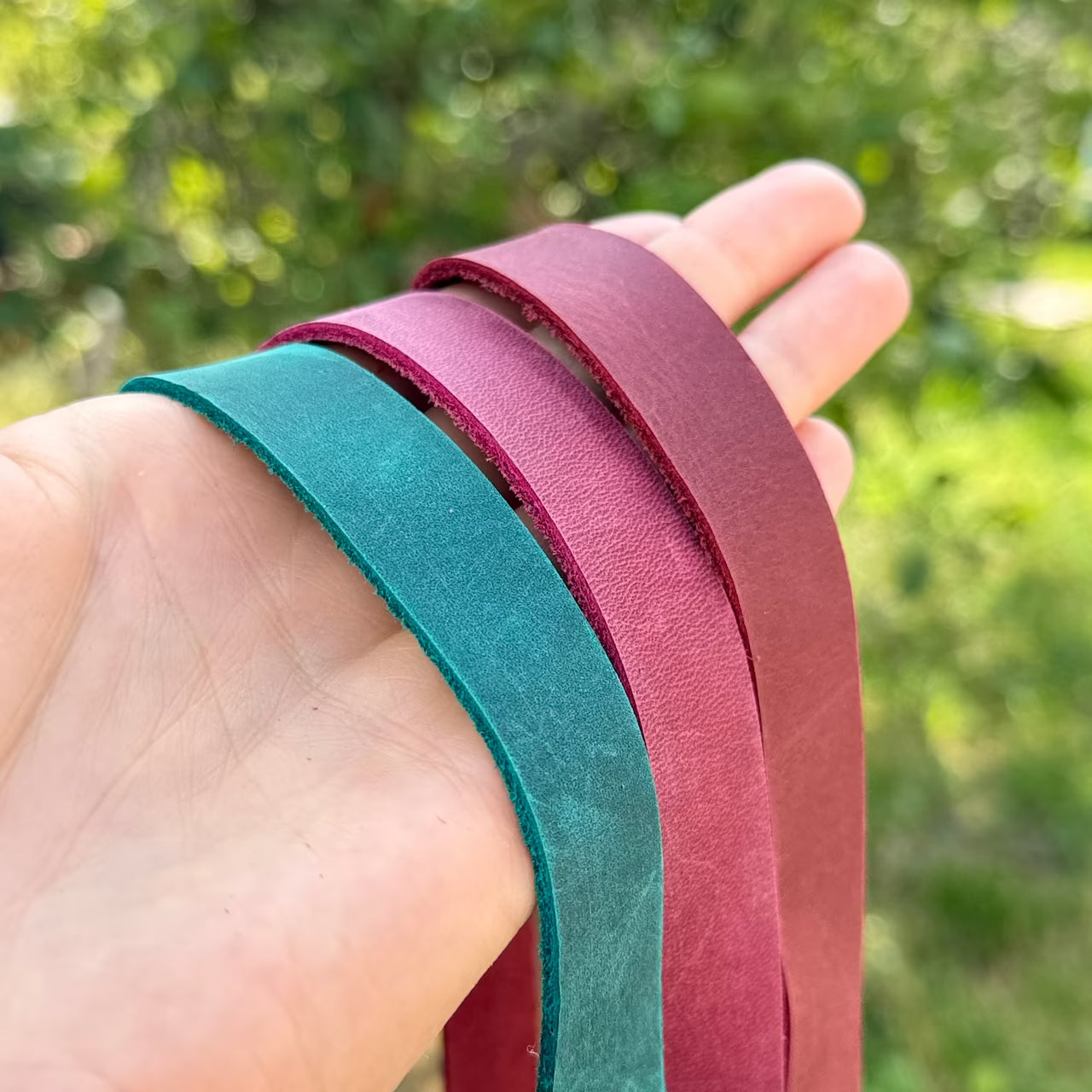 3 Lederbänder in petrol magenta und rot hängen über einer Hand mit der glatten Seite sichtbar