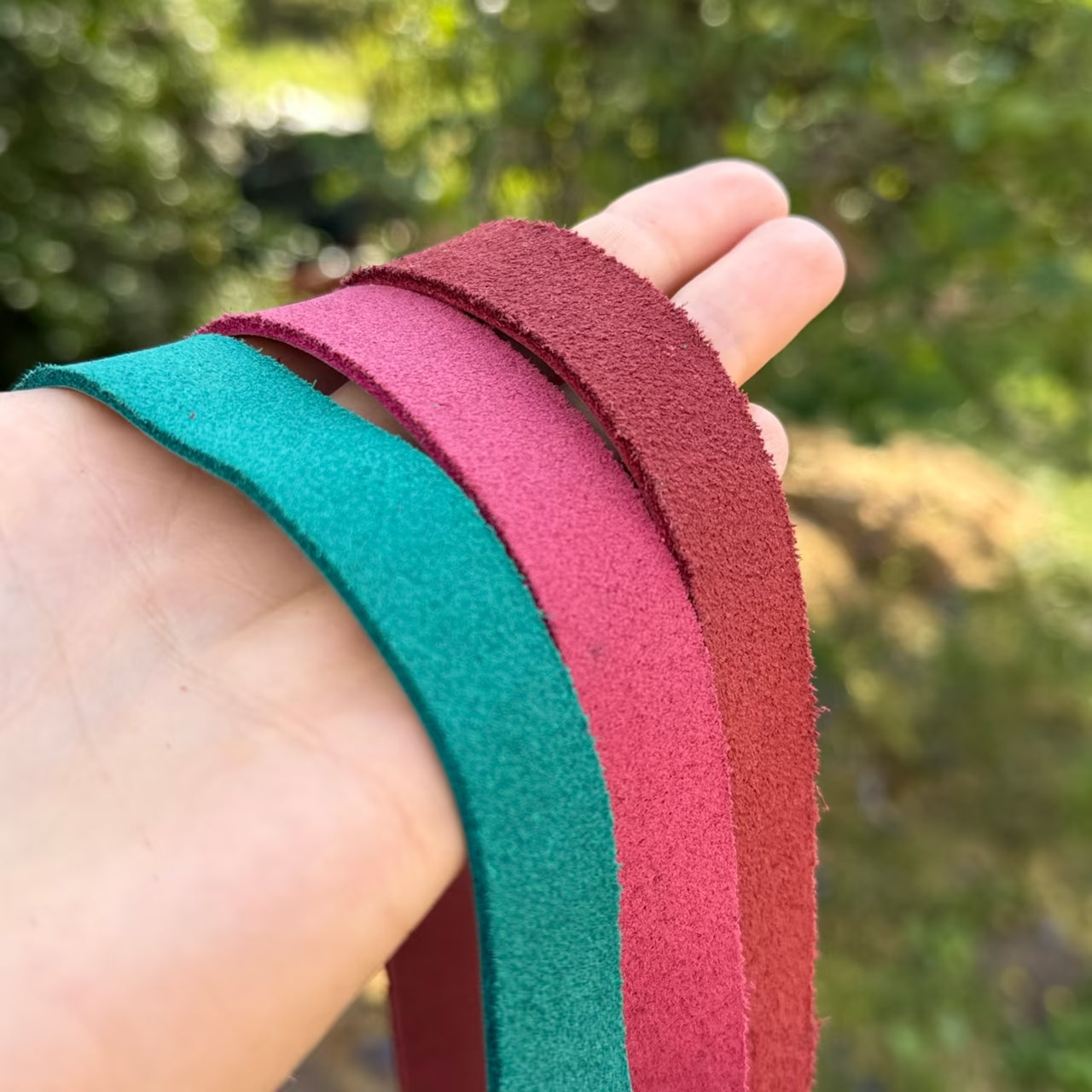3 Lederbänder in petrol, magenta und rot hängen über einer Hand mit der Wildlederseite sichtbar