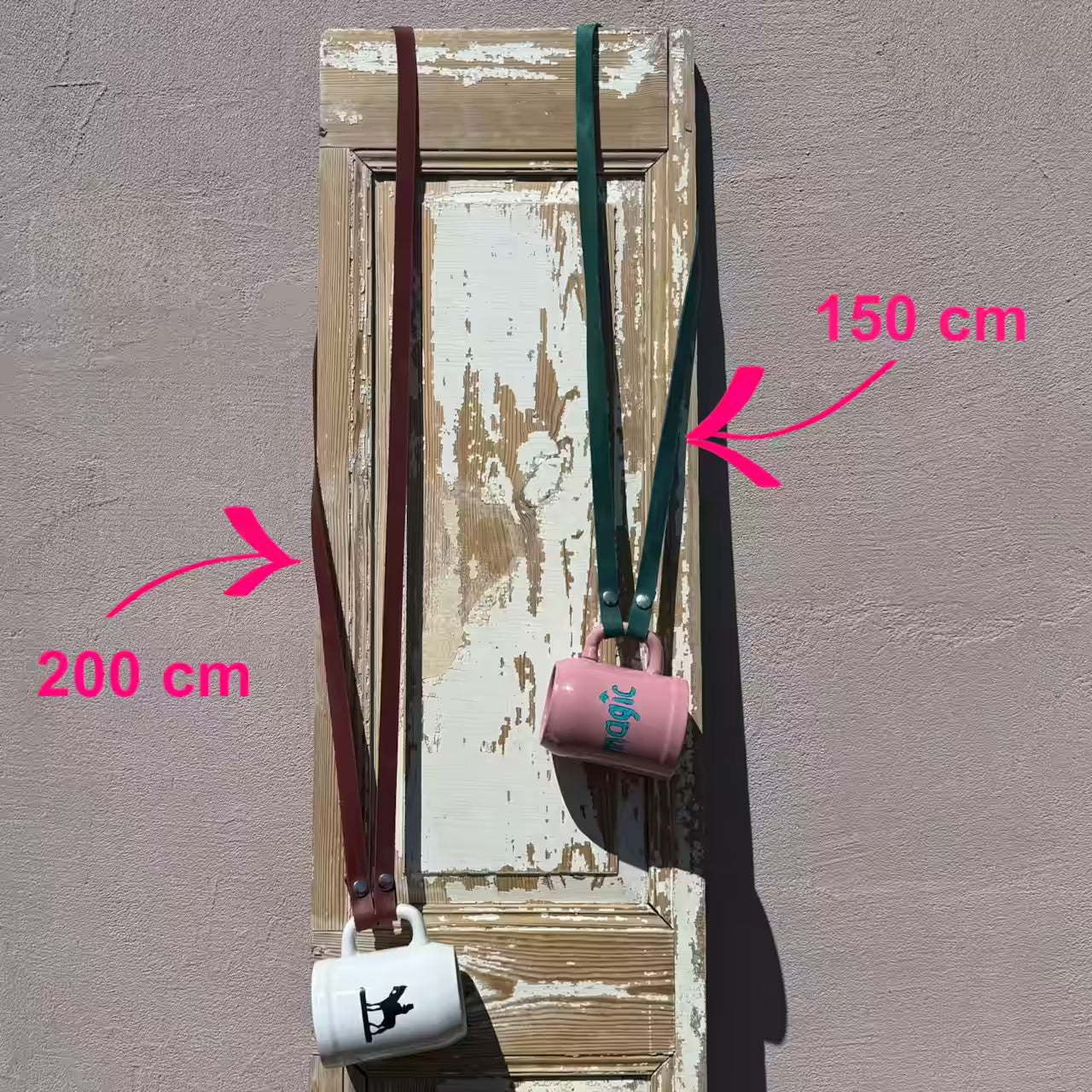 Ein weißer und ein rosa Krug hängen an einem roten längeren Lederband und einem petrol kürzerem Lederband. Beschriftung mit 200 cm des längeren Bandes und 150 cm des kürzeren Bandes