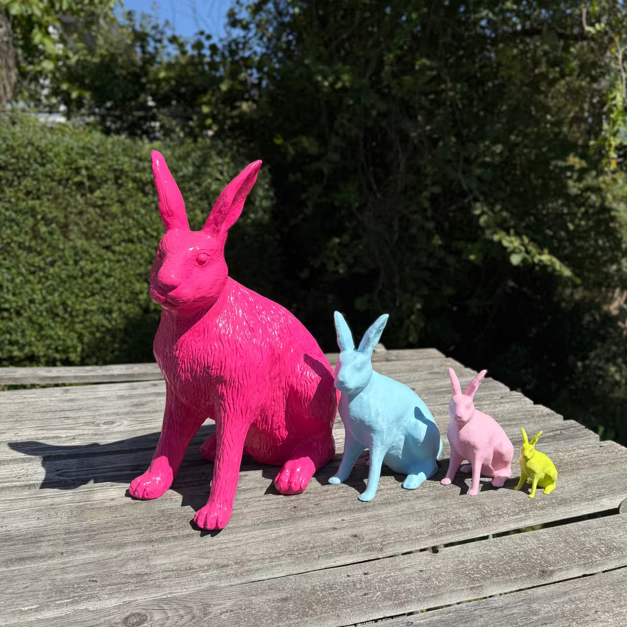 Neonpinker, blauer, rosa und limettengrüner Hase in Größenabstufung stehen auf Holzpalette