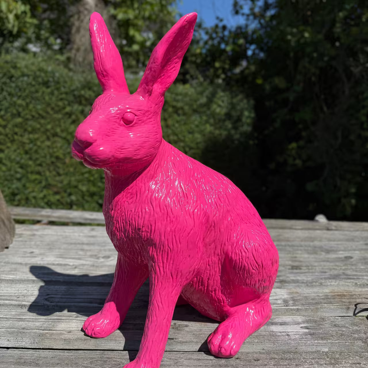 neonpinker Hase aus Kunstharz sitzt auf Holz