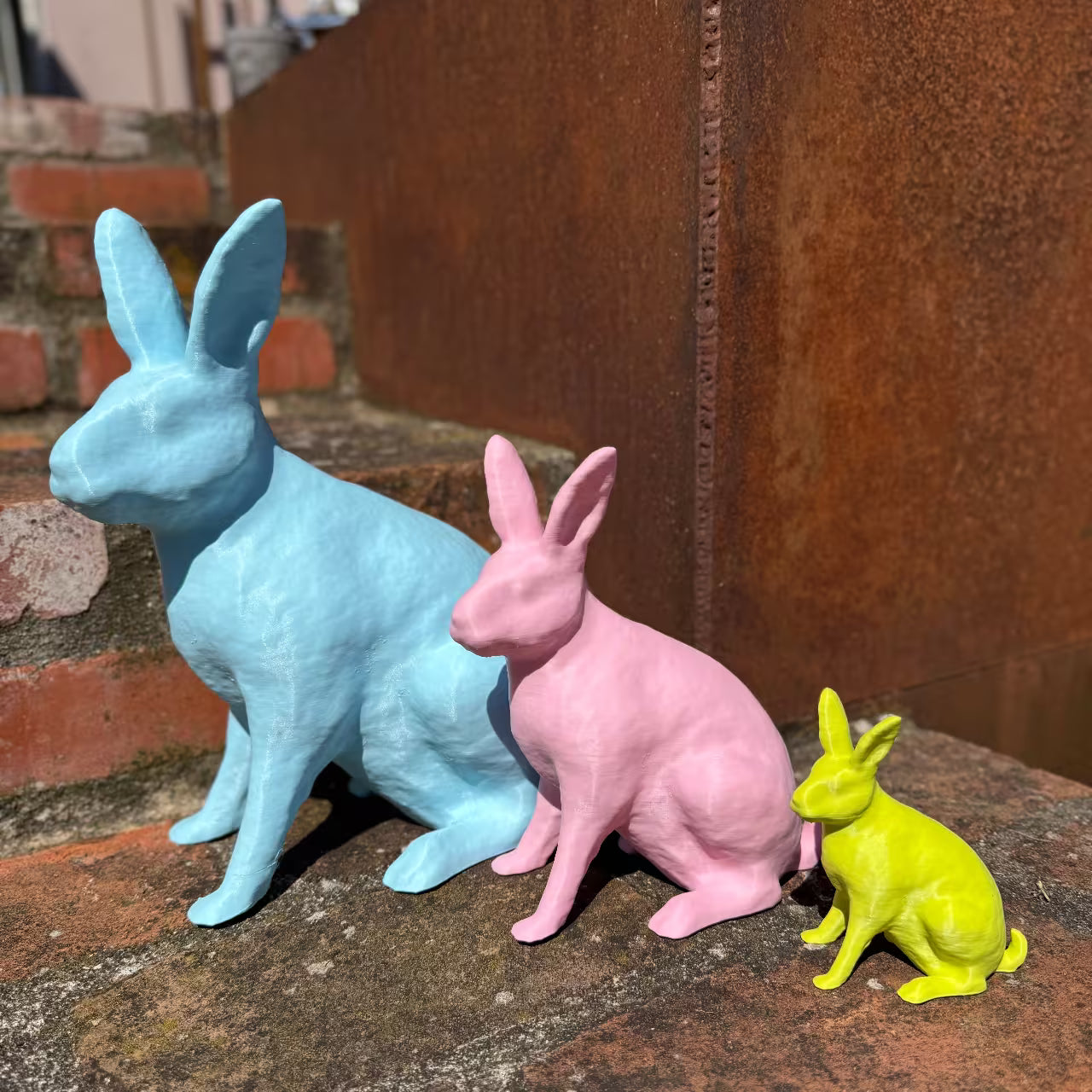 Ein blauer, rosa und limettengrüner Hase sitzen auf Steintreppe