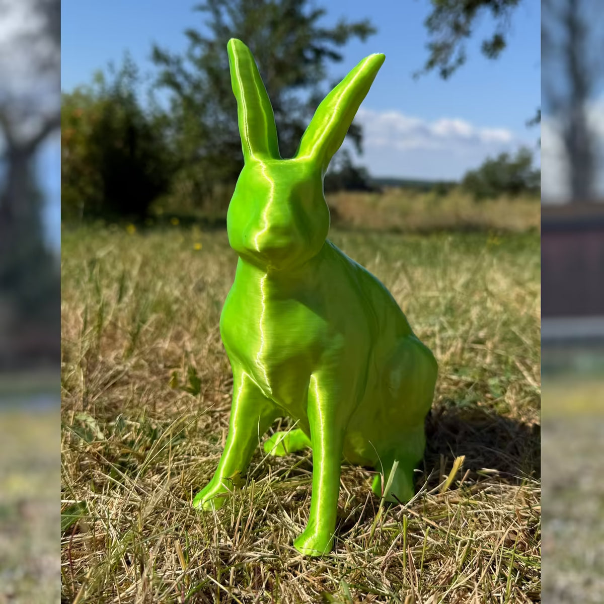 3D-gedruckter Hase in glänzendem grün sitzt im Gras
