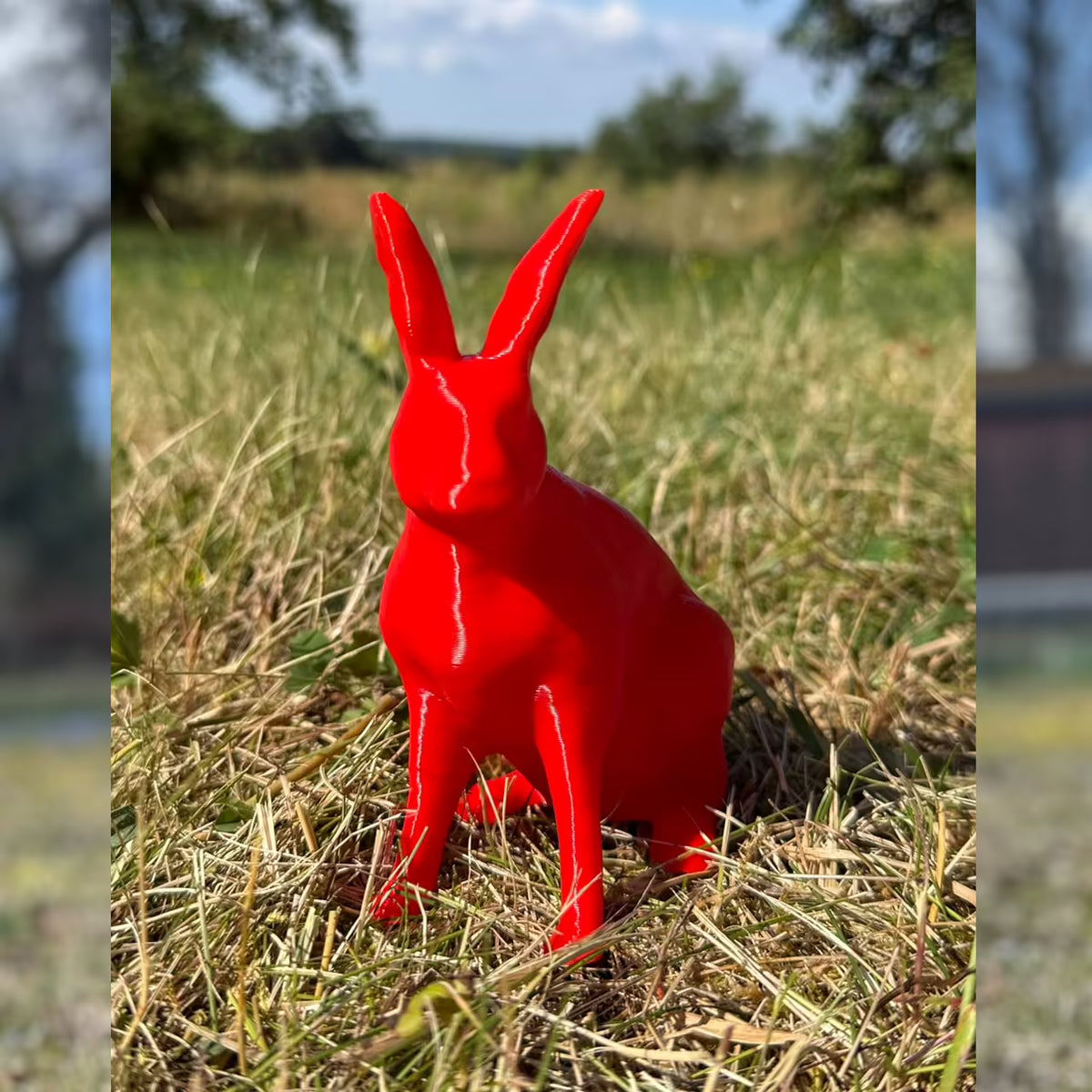 3D-gedruckter Hase in glänzendem rot sitzt im Gras