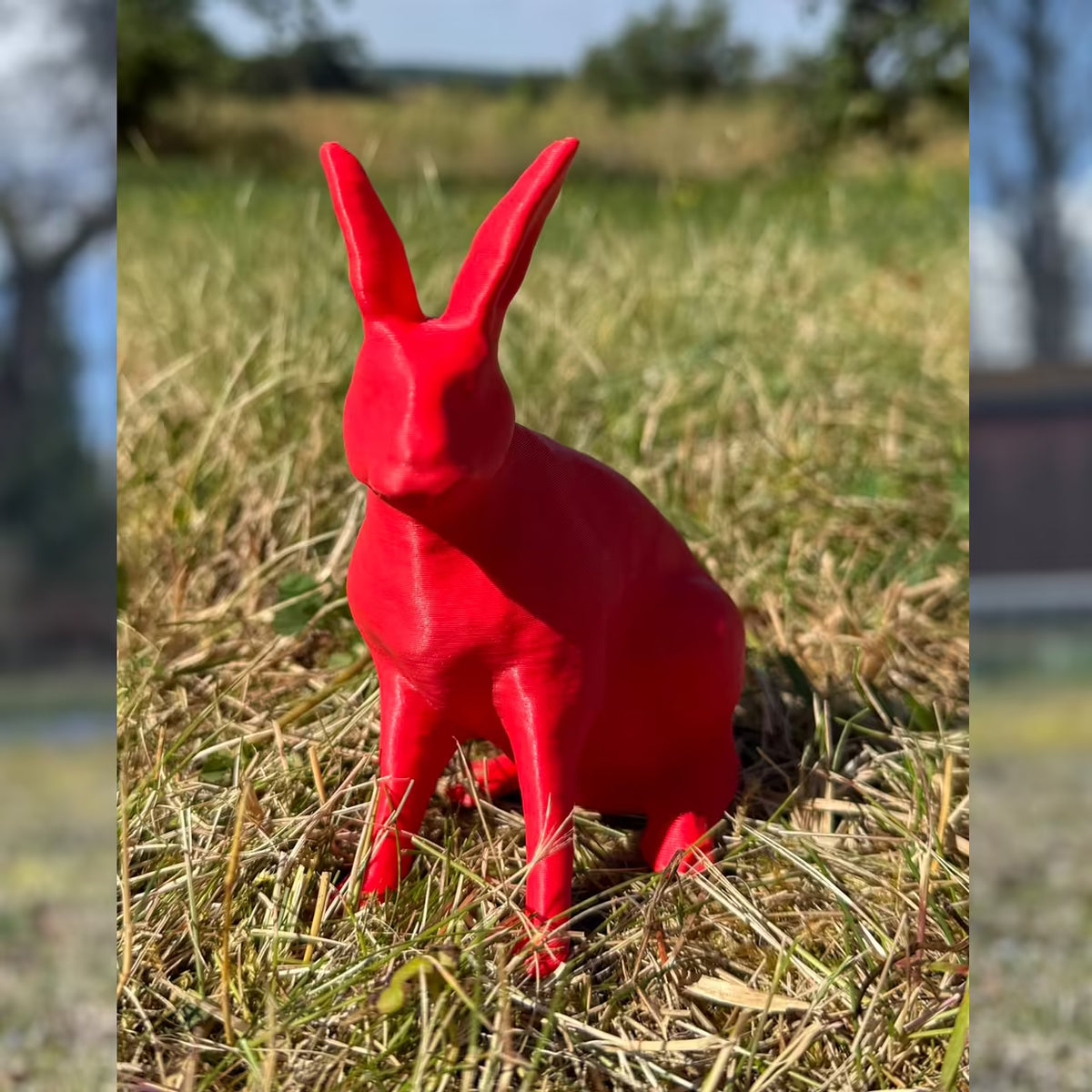 3D-gedruckter Hase in mattem rot sitzt im Gras