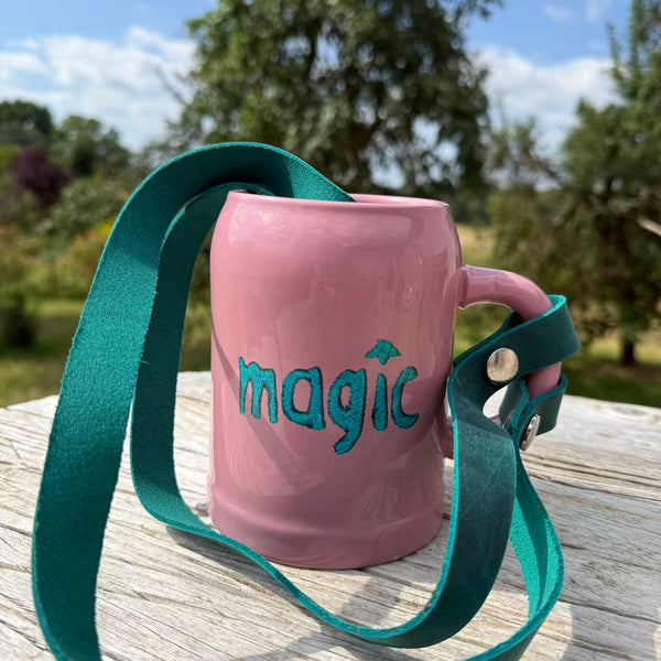 Rosa Bierkrug mit Aufschrift magic mit petrol Lederband am Henkel steht in der Natur