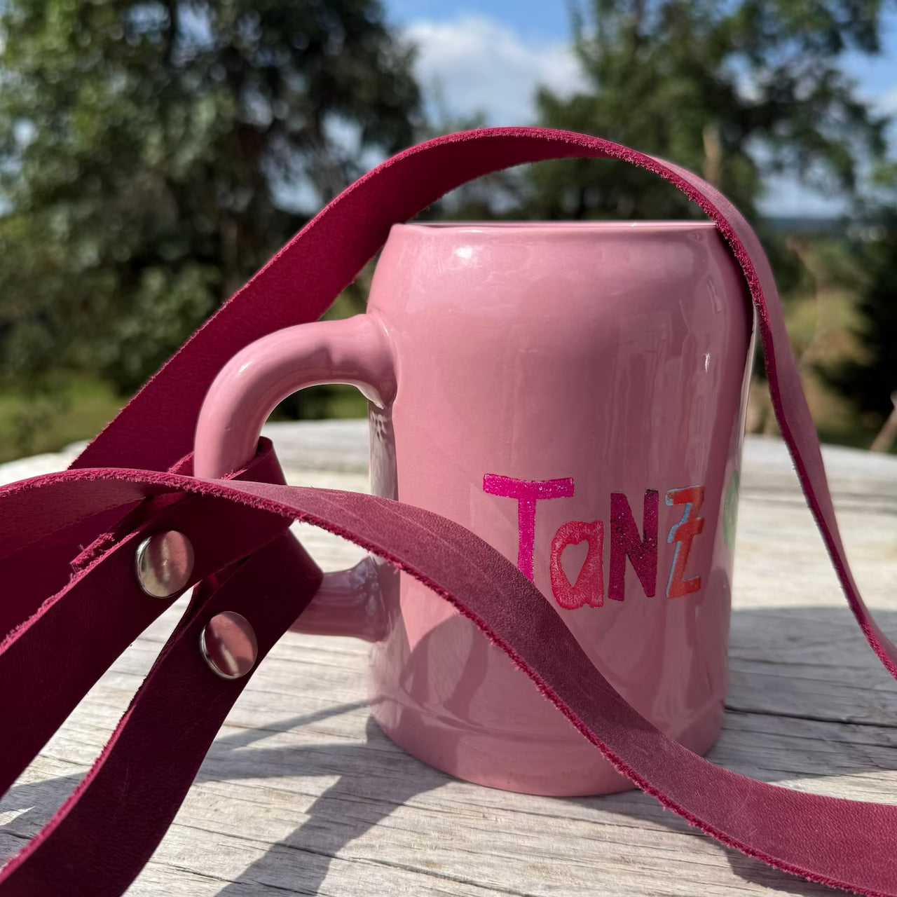 Rosa Bierkrug mit Aufschrift Tanz mit magenta Lederband am Henkel steht in der Natur