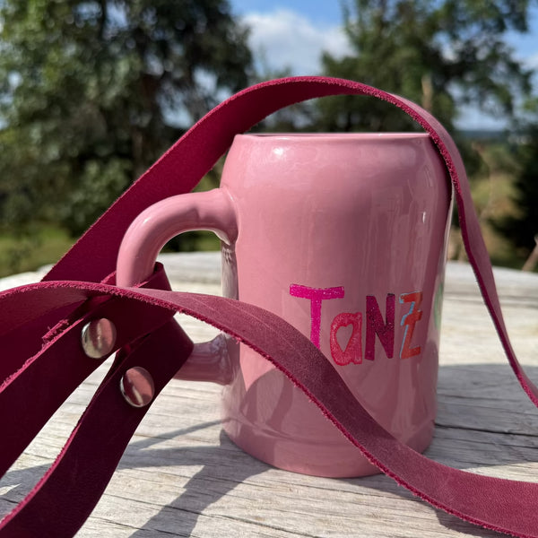 Rosa Bierkrug mit Aufschrift Tanz mit magenta Lederband am Henkel steht in der Natur