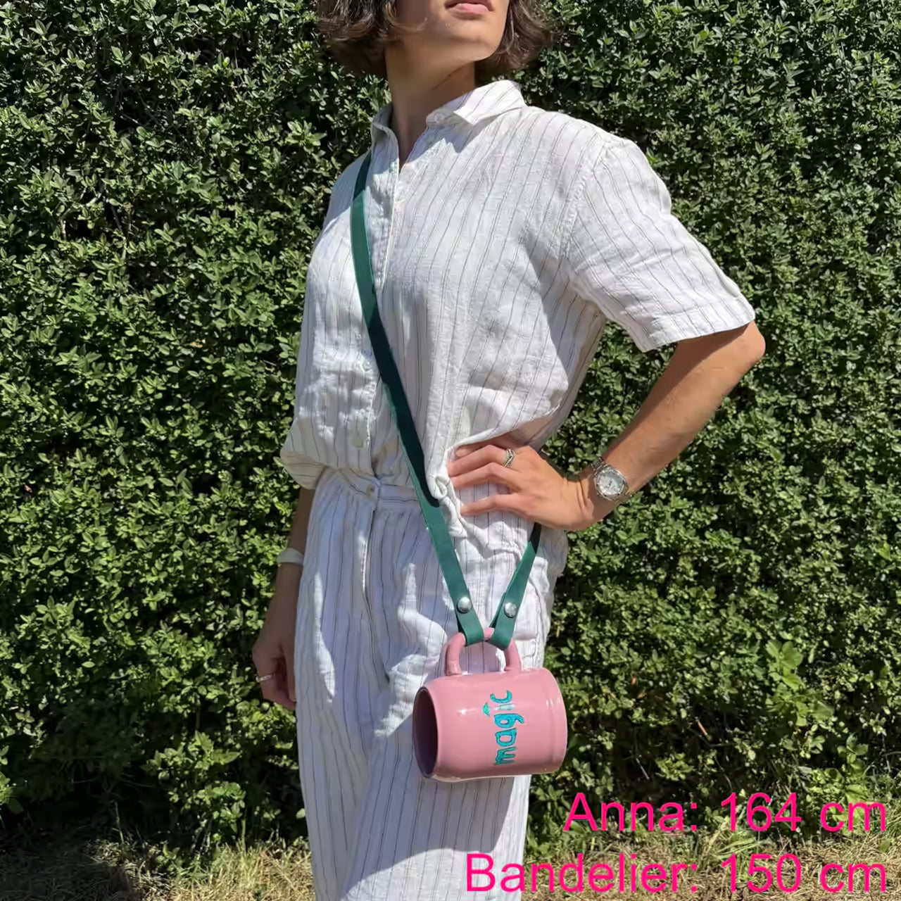 Model mit rosa Krug und petrol Lederband umgehängt steht in der Natur. Beschriftet mit "Anna: 164 cm, Bandelier: 150 cm"