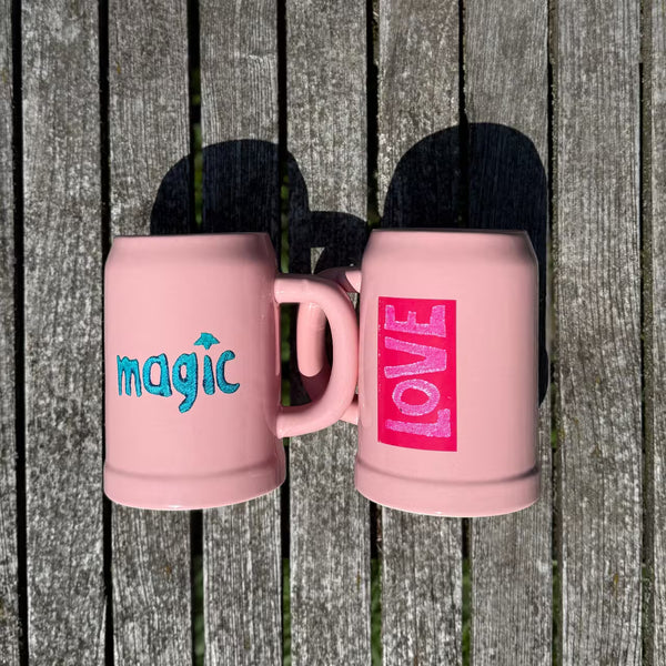 Zwei rosa Bierkrüge mit love und magic Print liegen auf Holztisch