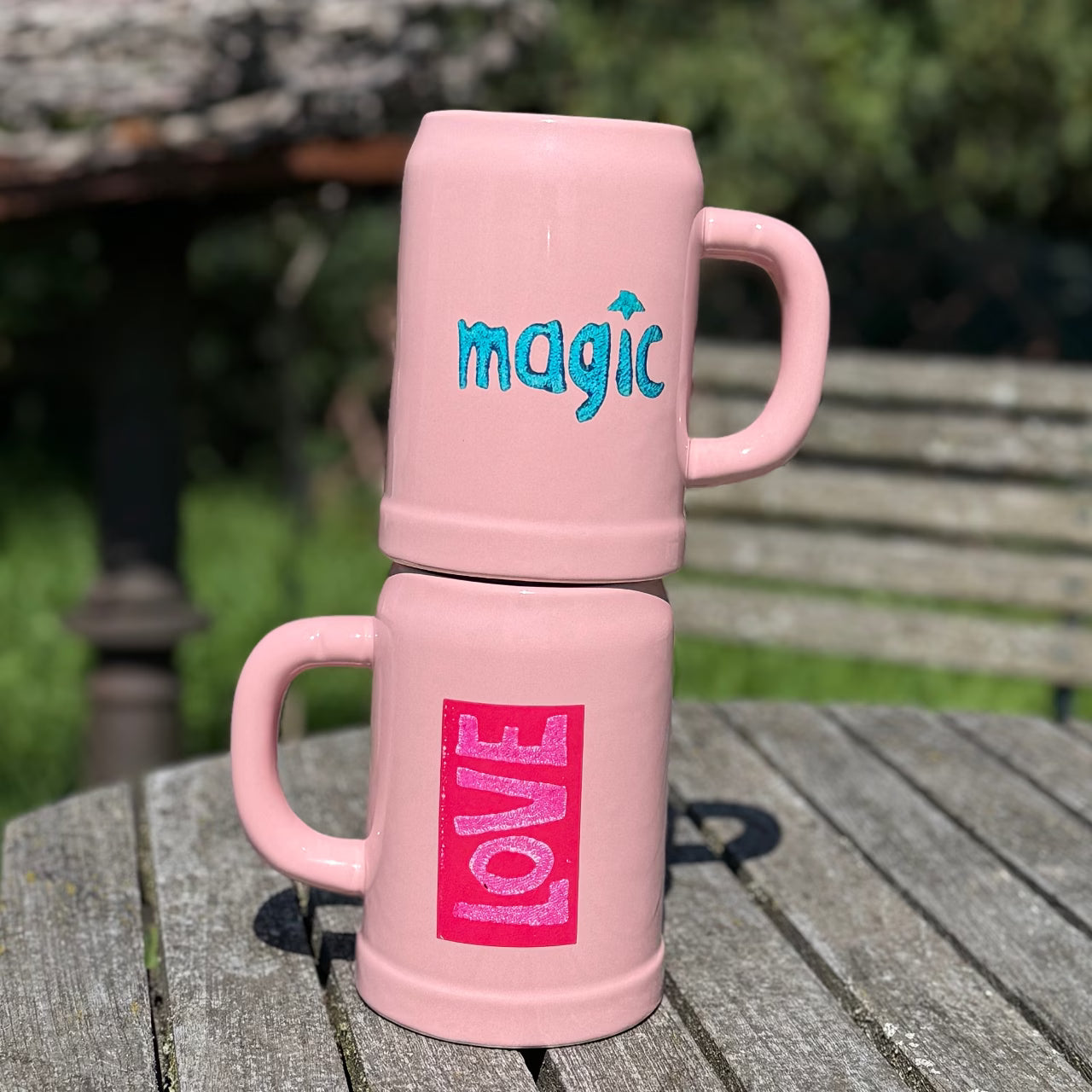 Zwei rosa Bierkrüge mit love und magic Print stehen auf Holztisch