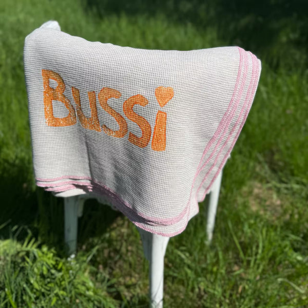Graue Decke mit orangenem Aufdruck Bussi hängt über Stuhl im Gras
