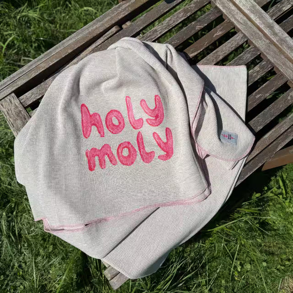 Graue Decke mit Aufdruck pinkem holy moly liegt auf Holzliege im Gras