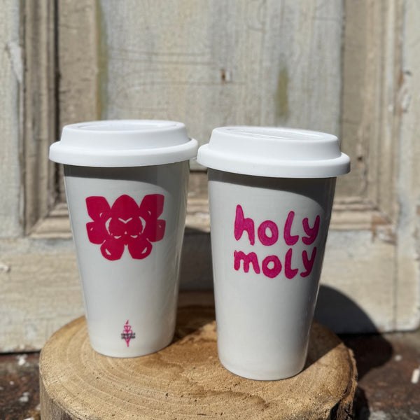 Zwei weiße To-Bo-Becher mit pinkem Blume und holy moly Print stehen auf Holz vor antiker Tür