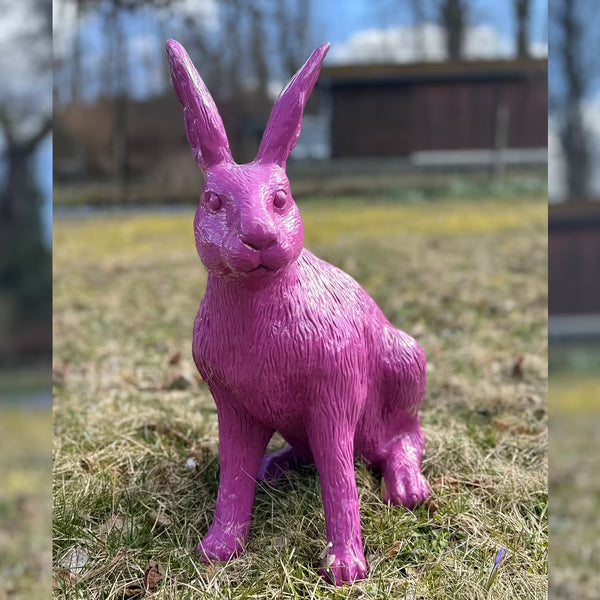 Rosa-Violette Hasenfigur sitzt im Gras