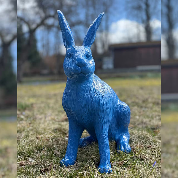 Himmelblaue Hasenfigur sitzt im Gras