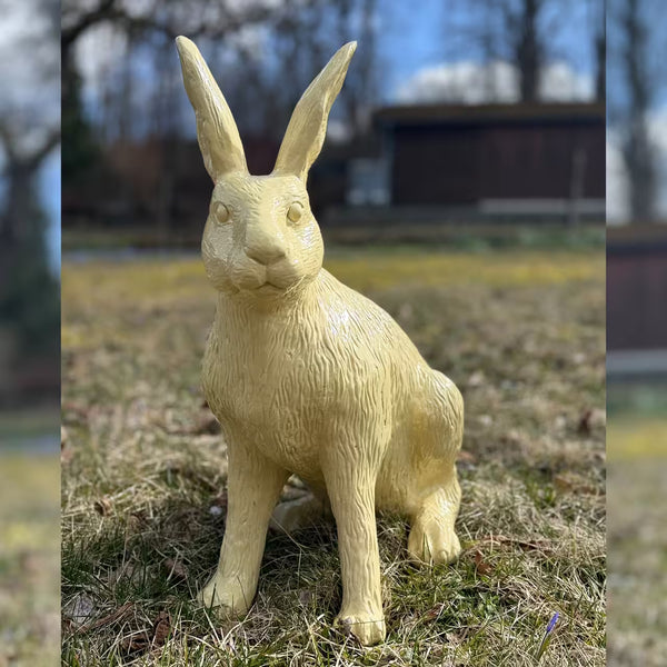 Elfenbeinfarbige Hasenfigur sitzt im Gras