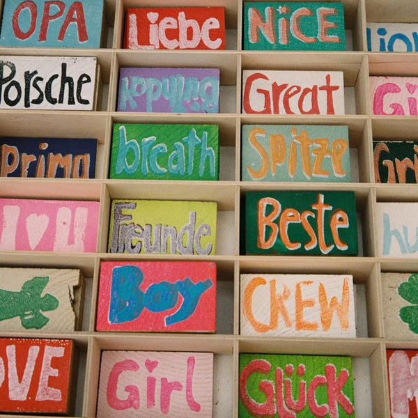 Holzstücke mit unterschiedlichen bunten Prints, wie z.B. Opa, Girl oder Spitze liegen in einem Setzkasten
