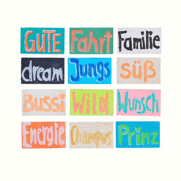 Übersicht über 12 Holztäfelchen in bunten Farben mit den Prints Gute, Fahrt, Familie, dream, Jungs, süß, Bussi, WIld, Wunsch, Energie, Champus, Prinz