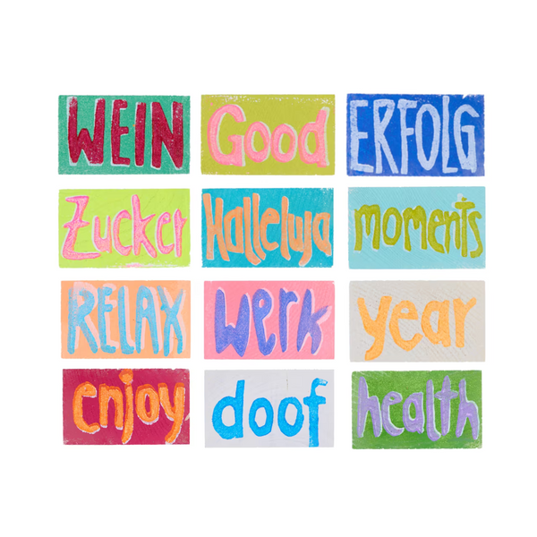 Übersicht über 12 Holztäfelchen in bunten Farben mit den Prints WEIN, Good, ERFOLG, Zucker, Halleluja, moments, RELAX, Werk, year, enjoy, doof, health